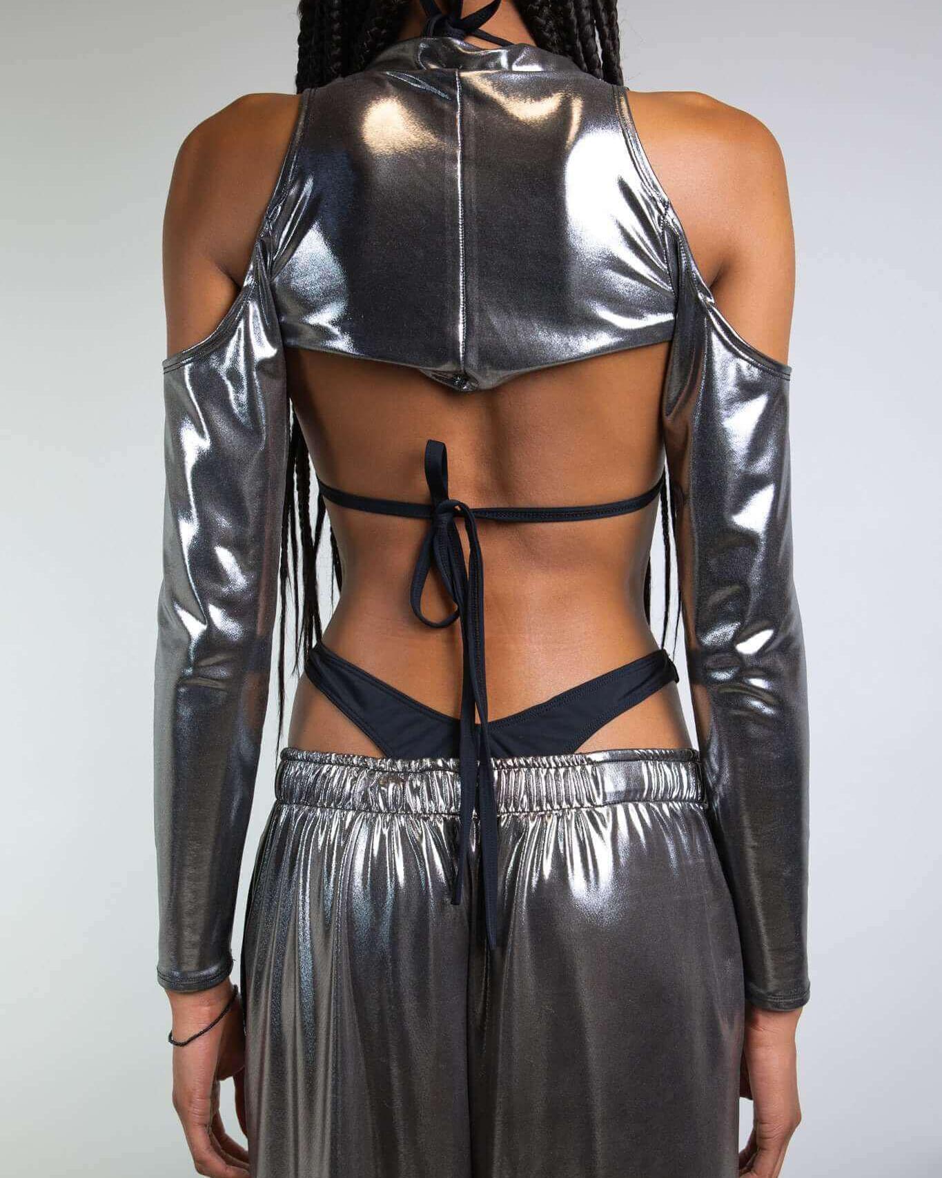 Woman wearing shiny chrome spectra sleeves with shoulder cutouts, showcasing a sleek back view, perfect for rave outfits.