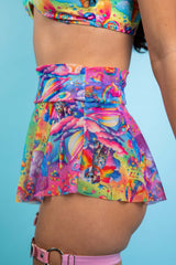 A girl wearing a rainbow crop top with whimsical characters on it and a matching mesh skirt. She is facing to the left.