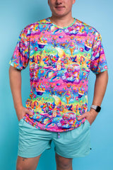 A man wearing a rainbow t shirt with whimsical characters on it and blue shorts.