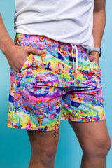 An up close photo of a man wearing rainbow shorts with whimsical characters and a white t-shirt.