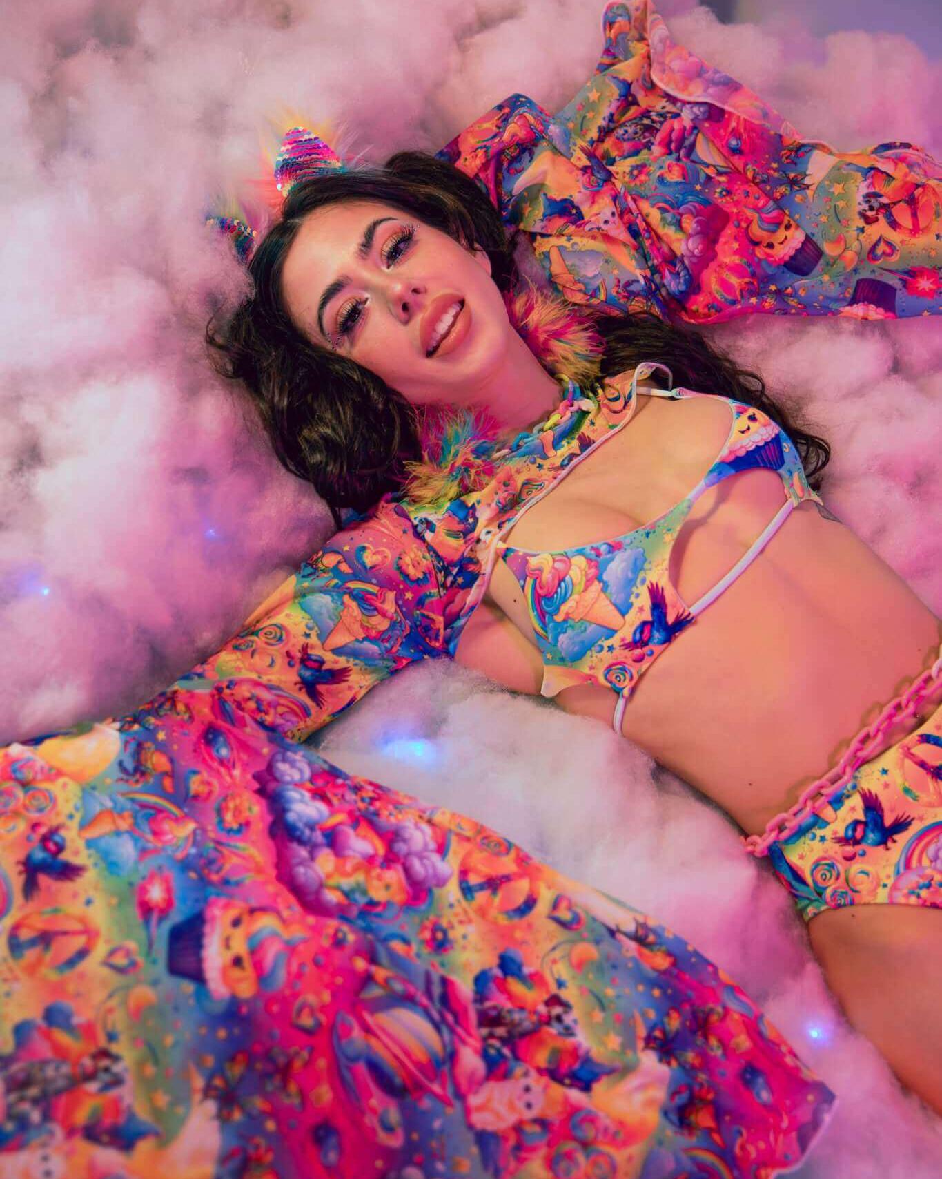 Model wearing vibrant Kosmic Mesh Bell Sleeves and colorful rave outfit, lying on fluffy clouds for a whimsical look.