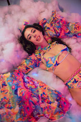 A woman laying in the clouds wearing a rainbow outfit.