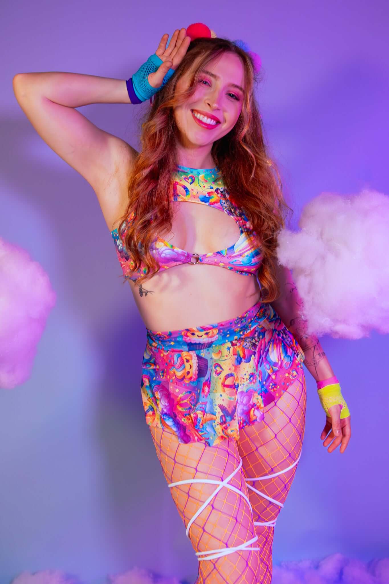 A girl wearing a rainbow crop top with whimsical characters on it and a matching mesh skirt.
