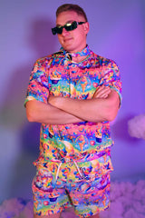 A man wearing a rainbow t shirt with whimsical characters on it and matching shorts.