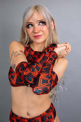 Model wearing Freedom Rave Wear's Labyrinth collection, highlighting a red geometric print with a front cut-out, matching sleeves, and coordinating bottoms.