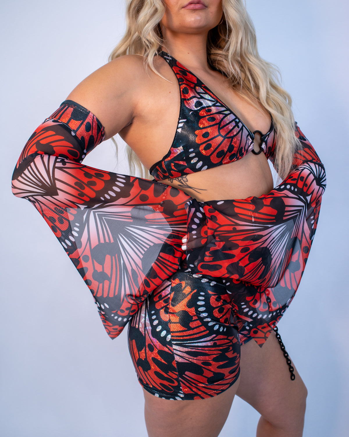 Front view of Lacewing Metamorphosis Sleeves in red and black gothic butterfly print, worn by a model at a rave.