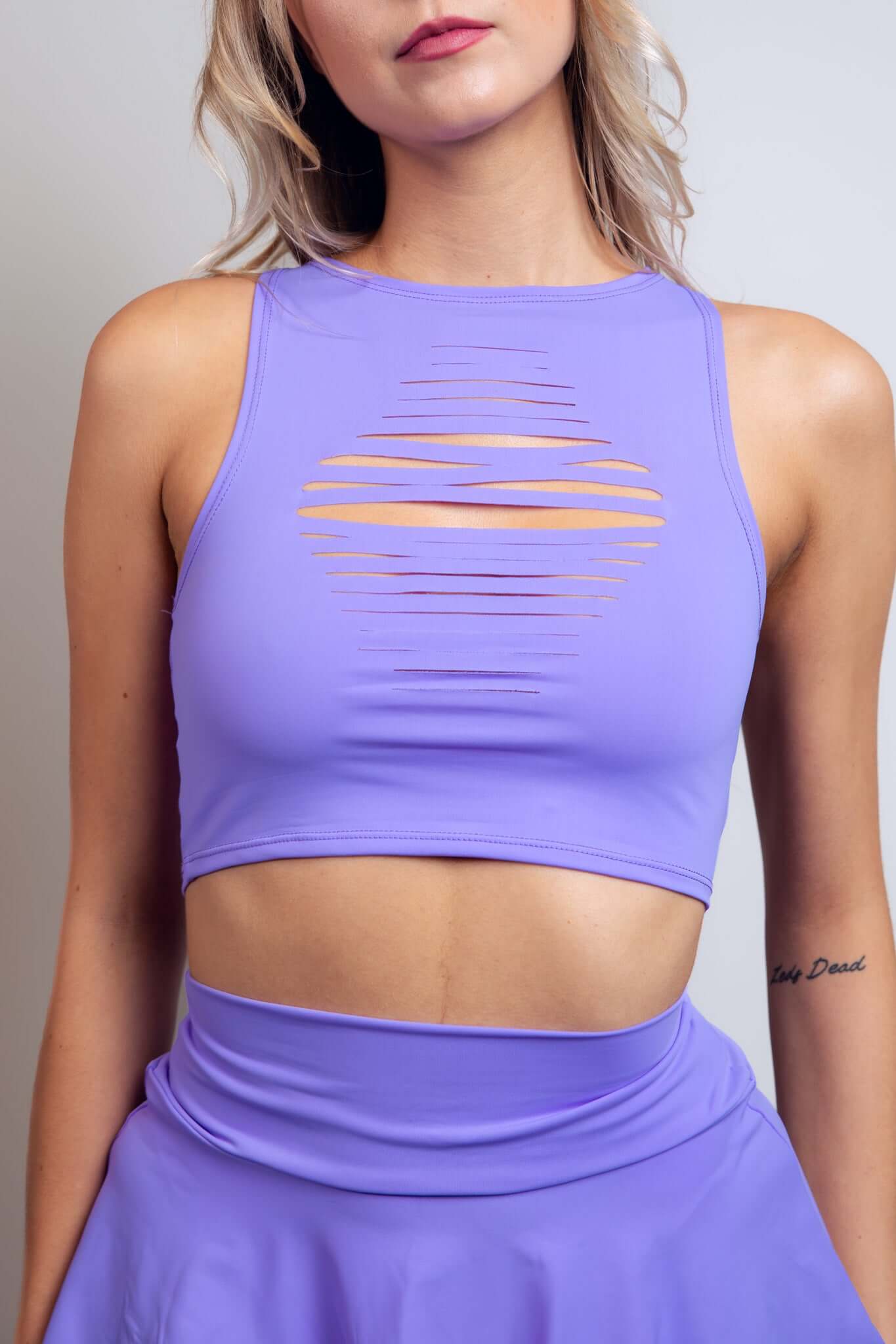 Close-up of a woman in a lavender Freedom Rave Wear crop top featuring a unique front slit design, paired with a matching high-waisted skirt.