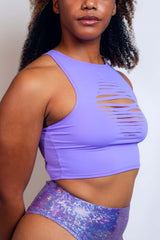 Side profile of a woman in a lavender Freedom Rave Wear crop top featuring bold slit details, paired with a sparkly purple high-waist rave bottom
