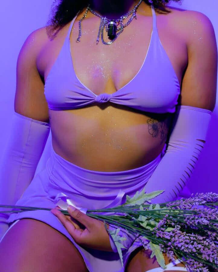 Model wearing a lavender supportive bikini top with lavender accents, holding lavender flowers, showcasing eco-friendly rave outfit.