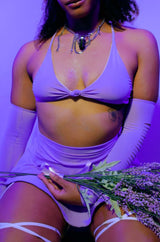 Woman in a lavender Freedom Rave Wear halter top with sparkling details, accessorized with chunky necklaces, holding a bouquet of lavender, under purple lighting