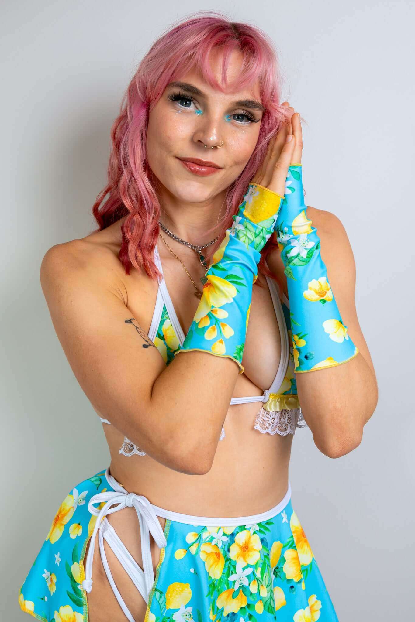 Model in a floral two-piece rave outfit from Freedom Rave Wear: triangle top with lace trim, high-waisted skirt, and matching sleeves.