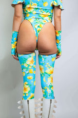 Back view of a model in a floral rave outfit from Freedom Rave Wear: blue and yellow high-waisted bottoms, matching thigh-high leggings, and white platform boots.