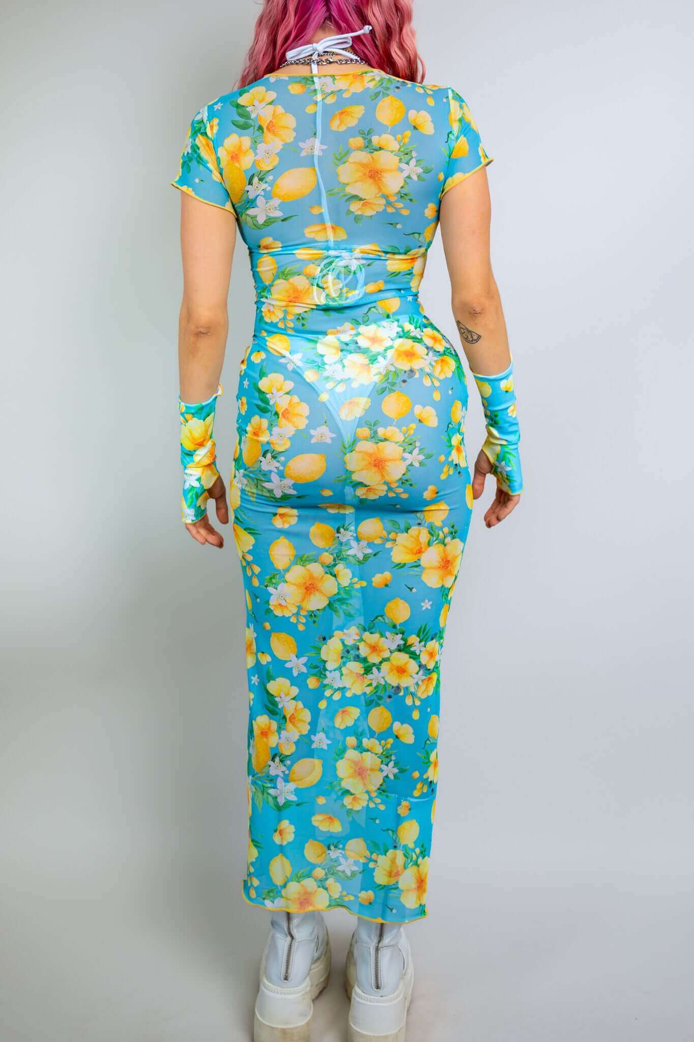  Back view of a model in a floral mesh dress from Freedom Rave Wear: blue and yellow full-length dress with matching sleeves, showcasing vibrant floral patterns.