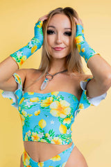 Model in a floral three-piece rave outfit from Freedom Rave Wear: off-shoulder top, high-waisted bottoms, and matching sleeves in blue and yellow.