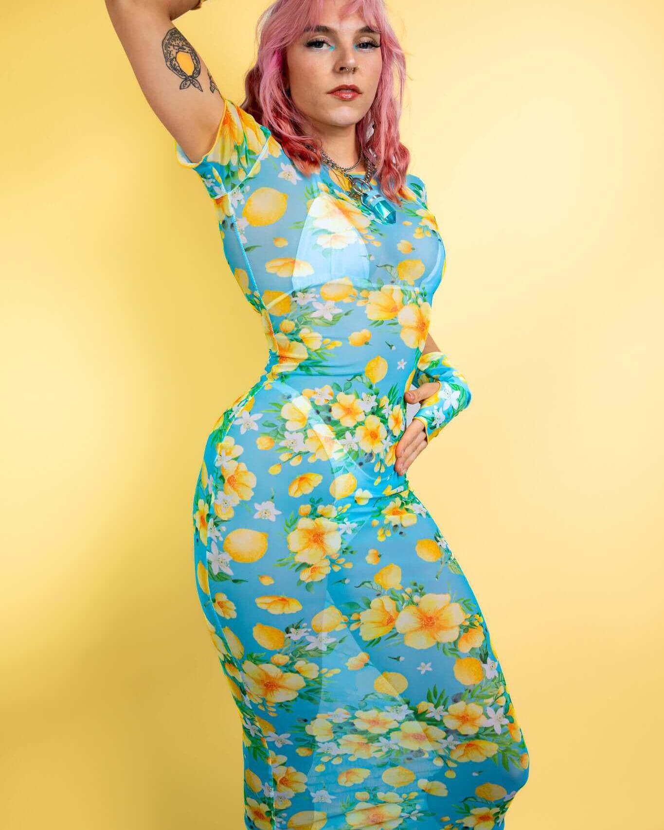 Model showcasing Lemon Drop Mesh Baby Tee Maxi Dress with floral design against a yellow background, perfect for rave outfits.