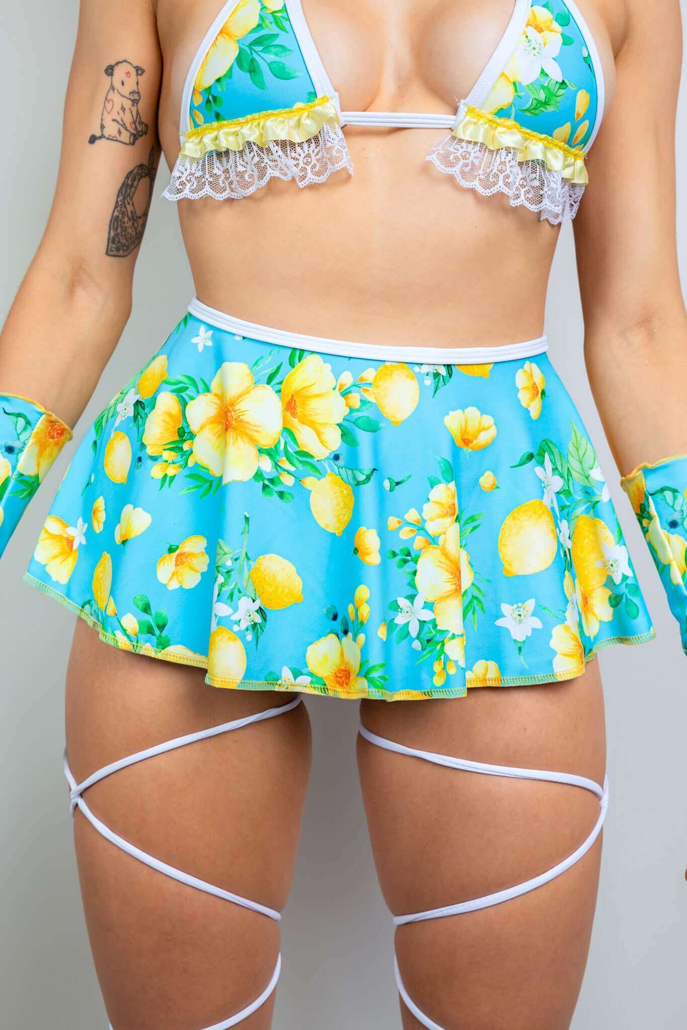 Close-up of Freedom Rave Wear's blue floral tie skirt, lace-trimmed bikini top, and strappy leg accessories in a vibrant yellow flower print.