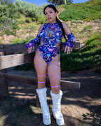 Woman wearing Lucent rave bodysuit with side cutouts and purple leg straps sitting outdoors for festival outfit styling