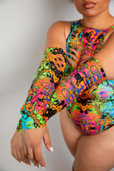 Close-up of a model in a vibrant, neon printed Freedom Rave Wear bodysuit, focusing on the intricate arm patterns and cut-out details