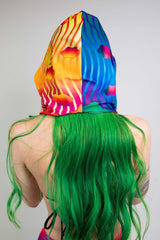 Freedom Rave Wear's colorful rave hood with sunset and wave patterns, showcased on a model with vibrant green hair, enhances any festival look