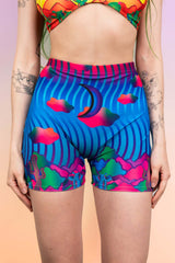 Woman wearing Freedom Rave Wear high-waisted shorts with dynamic, multicolored waves and psychedelic cloud prints.