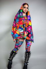 A girl with swirly black eye makeup wearing a rainbow patchwork bodysuit with a matching pashmina draped over her head.