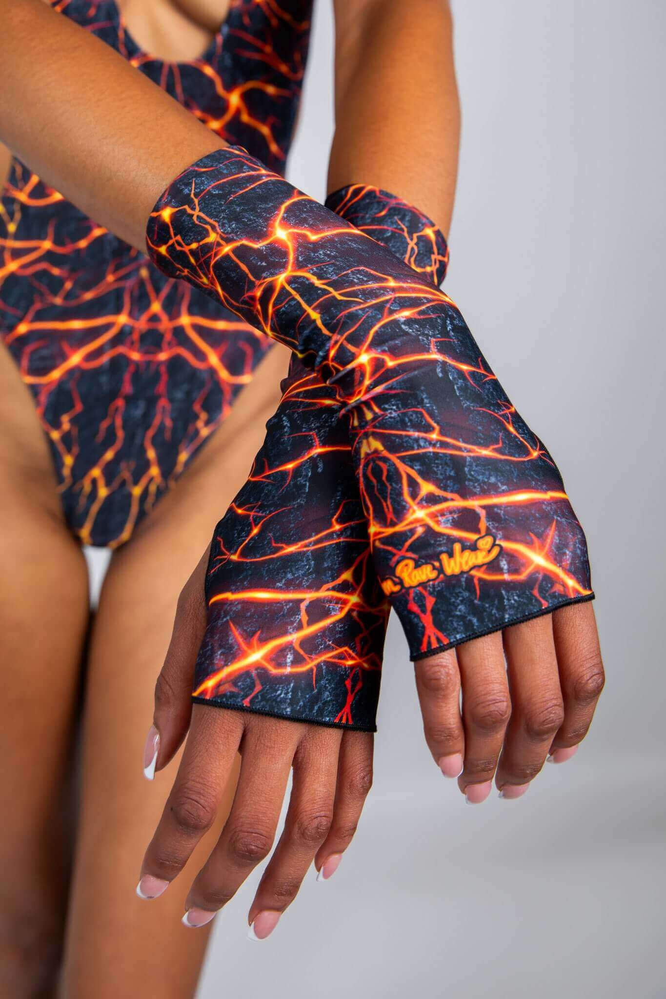 Close-up of model wearing orange lightning print fingerless gloves and matching bodysuit from Freedom Rave Wear, highlighting rave-inspired details.