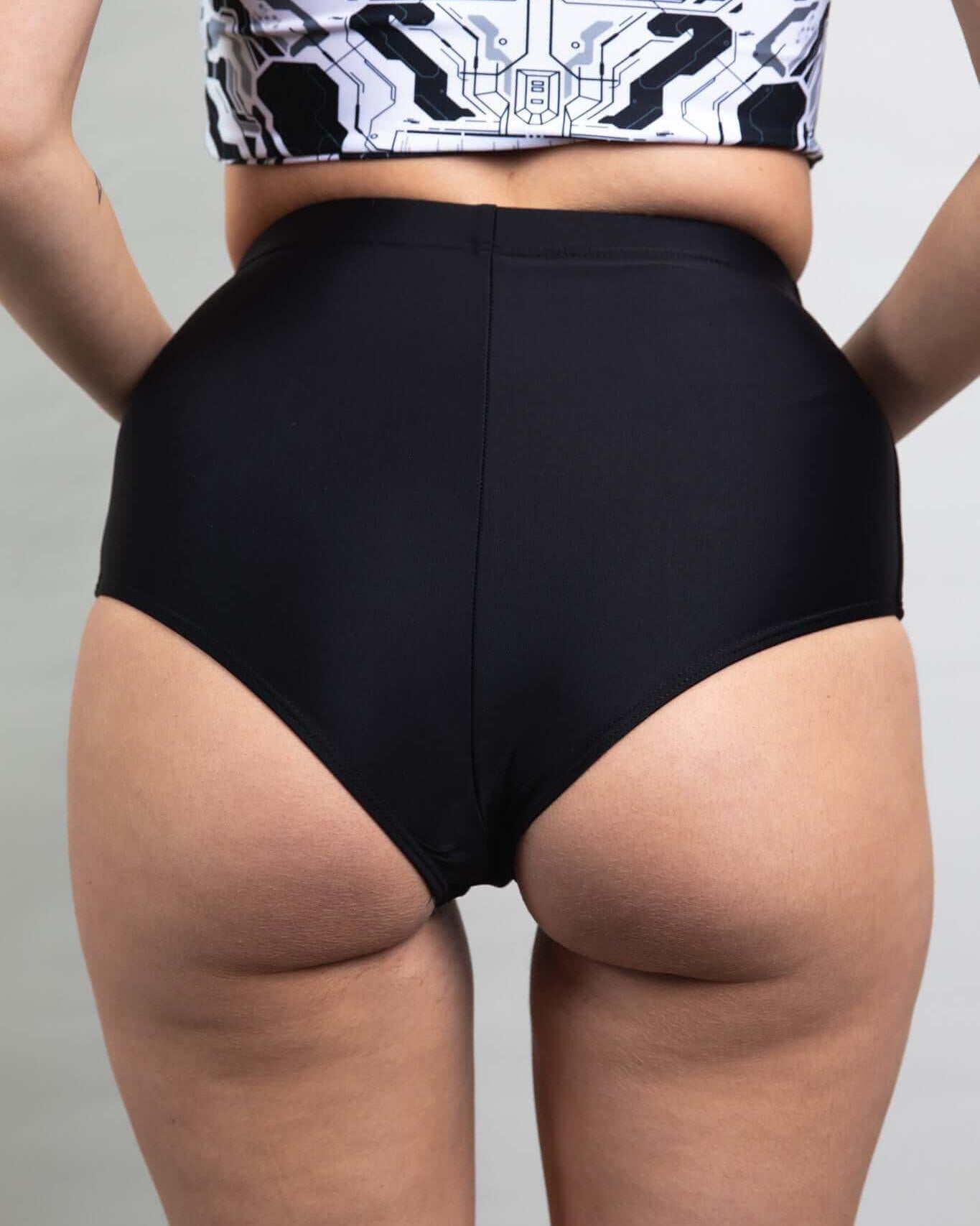 Woman wearing matte black high waisted bottoms, showcasing cheeky back design, perfect for rave outfits.