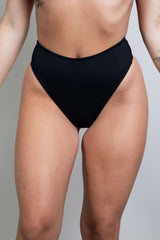 Matte black high waisted thong, perfect for rave outfits, showcasing a cheeky cut and recycled material design.