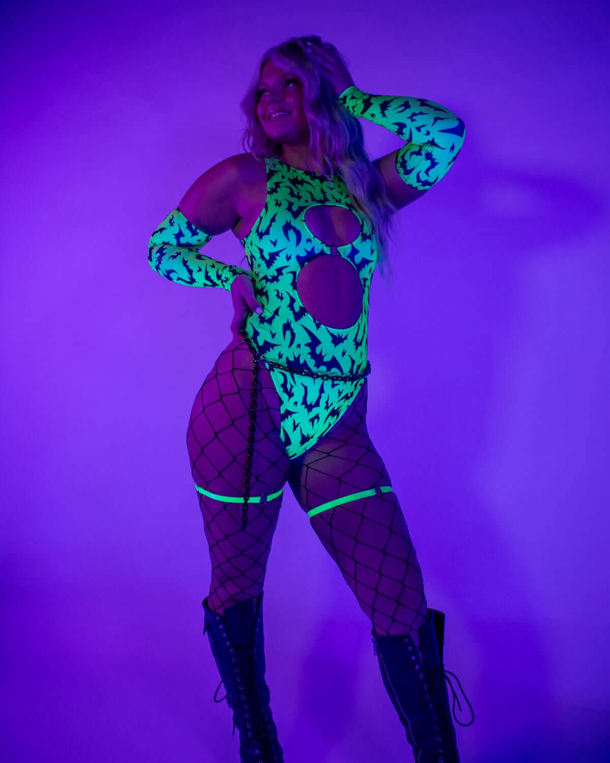 Model wearing OG Batty Keyhole Bodysuit - UV Green, featuring glow-in-the-dark bat print and stylish fishnet stockings.
