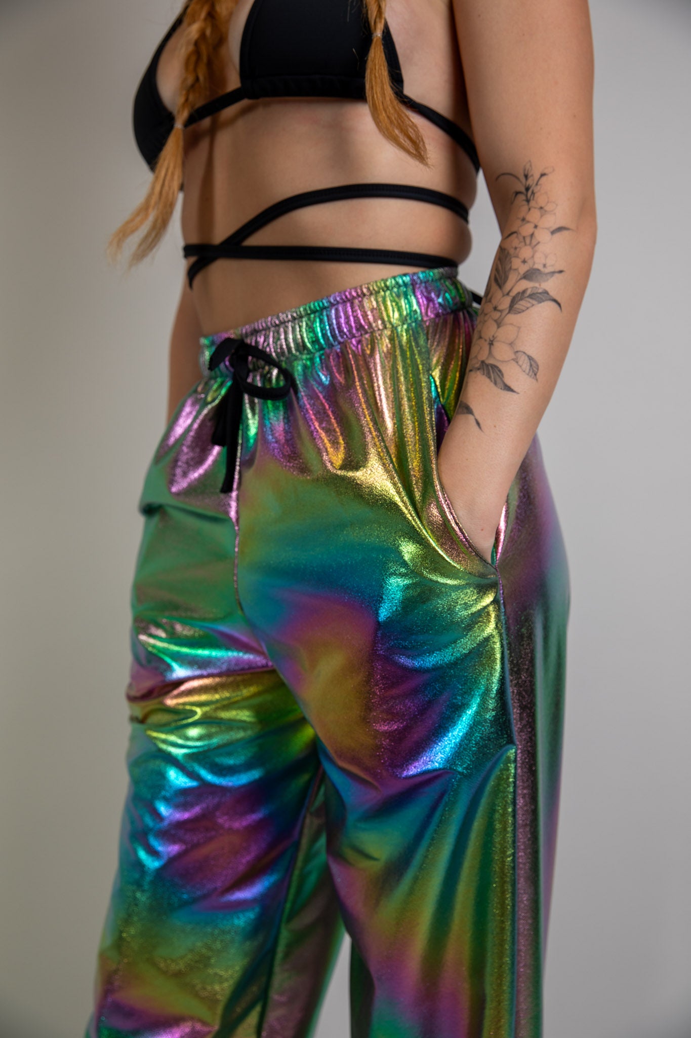 Holographic high-waisted rave pants, angled front view, vibrant swirl pattern, paired with black crop top, perfect for festival or party wear.