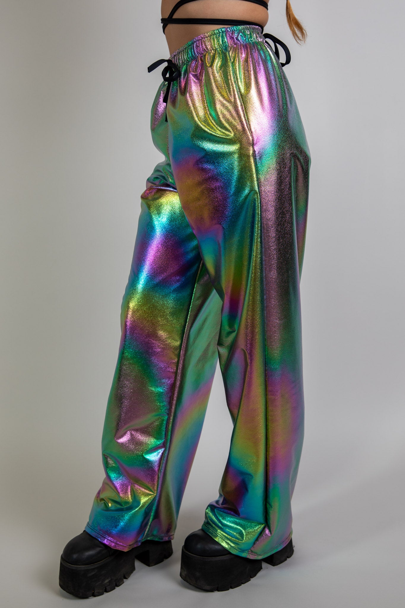 Side view of holographic swirl print high-waisted rave pants, showcasing relaxed fit and reflective multicolor fabric, festival-ready style.