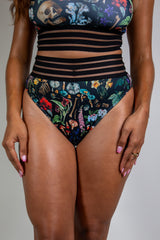 Front view of model wearing Poison Sporty Bottoms with a vibrant abstract design on black fabric, high-waisted cut, perfect for rave and festival fashion.