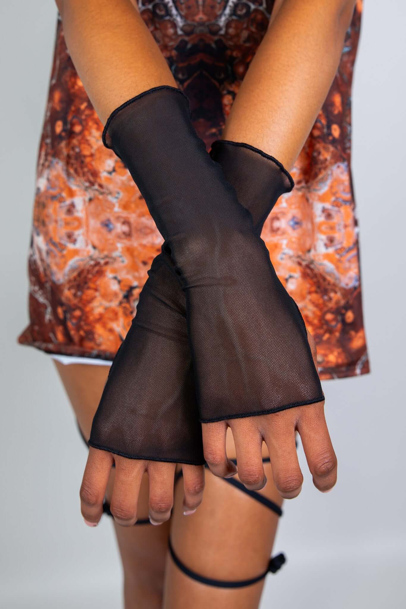 Close-up of black mesh gloves from Freedom Rave Wear, featuring a sheer, fingerless design that extends past the wrist, paired with a festival outfit.