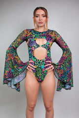 Confident woman in a vibrant Freedom Rave Wear bodysuit with dramatic cutouts, bell sleeves, and colorful psychedelic patterns.