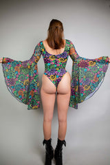 Rear view of a model in a Freedom Rave Wear Goddess bodysuit with a bold psychedelic print and flowy sleeves, paired with sleek black boots, ready for a rave.
