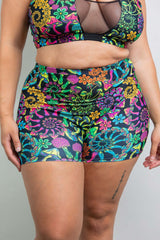 Close-up of a model wearing Freedom Rave Wear high-waisted rave shorts, showcasing a vivid psychedelic print with multicolored floral and mushroom patterns. 