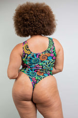 Back view of a model in Freedom Rave Wear's Psybloom bodysuit, highlighting the scooped back and colorful neon print, complemented by natural curly hair.