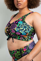 Close-up view of a model in Freedom Rave Wear's lace-up rave top featuring a vibrant, floral pattern and criss-cross detailing, paired with a matching festival bottom for a stylish rave look.