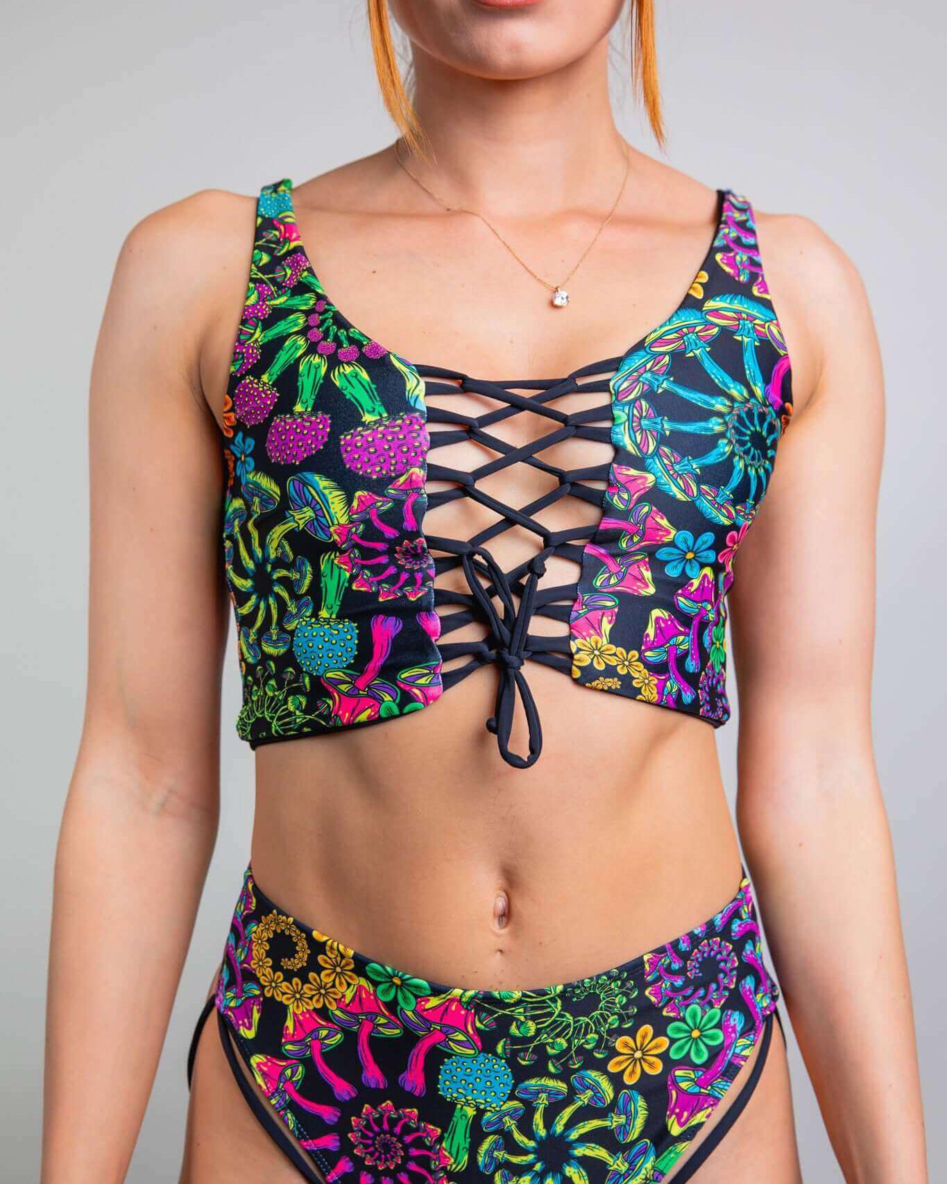 Model wearing the PsyBloom Lace Up Top, a vibrant crop top for rave outfits with colorful floral patterns and lace-up design.