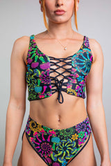 Model wearing Freedom Rave Wear's colorful floral lace-up bikini top and matching high-waisted bikini bottoms, designed with vivid patterns and bold colors for an eye-catching rave look.