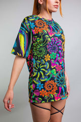 Model in Freedom Rave Wear's colorful oversized t-shirt featuring a vibrant, detailed psychedelic floral design, styled casually over high-waisted rave bottoms with criss-cross thigh straps.