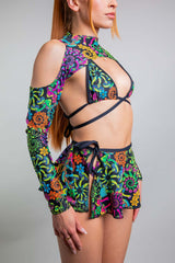 Side profile of a model in Freedom Rave Wear, featuring a crisscross bikini top and psychedelic print spectra sleeves, tied together with a high-waist skirt.