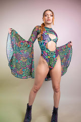 Dynamic pose of a woman in a Freedom Rave Wear bodysuit featuring vibrant floral designs with peekaboo cutouts and flowing bell sleeves.