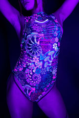 Dynamic pose of a model in a Freedom Rave Wear Psybloom bodysuit, highlighted by neon lighting that accentuates the psychedelic print and edgy side cut-outs.