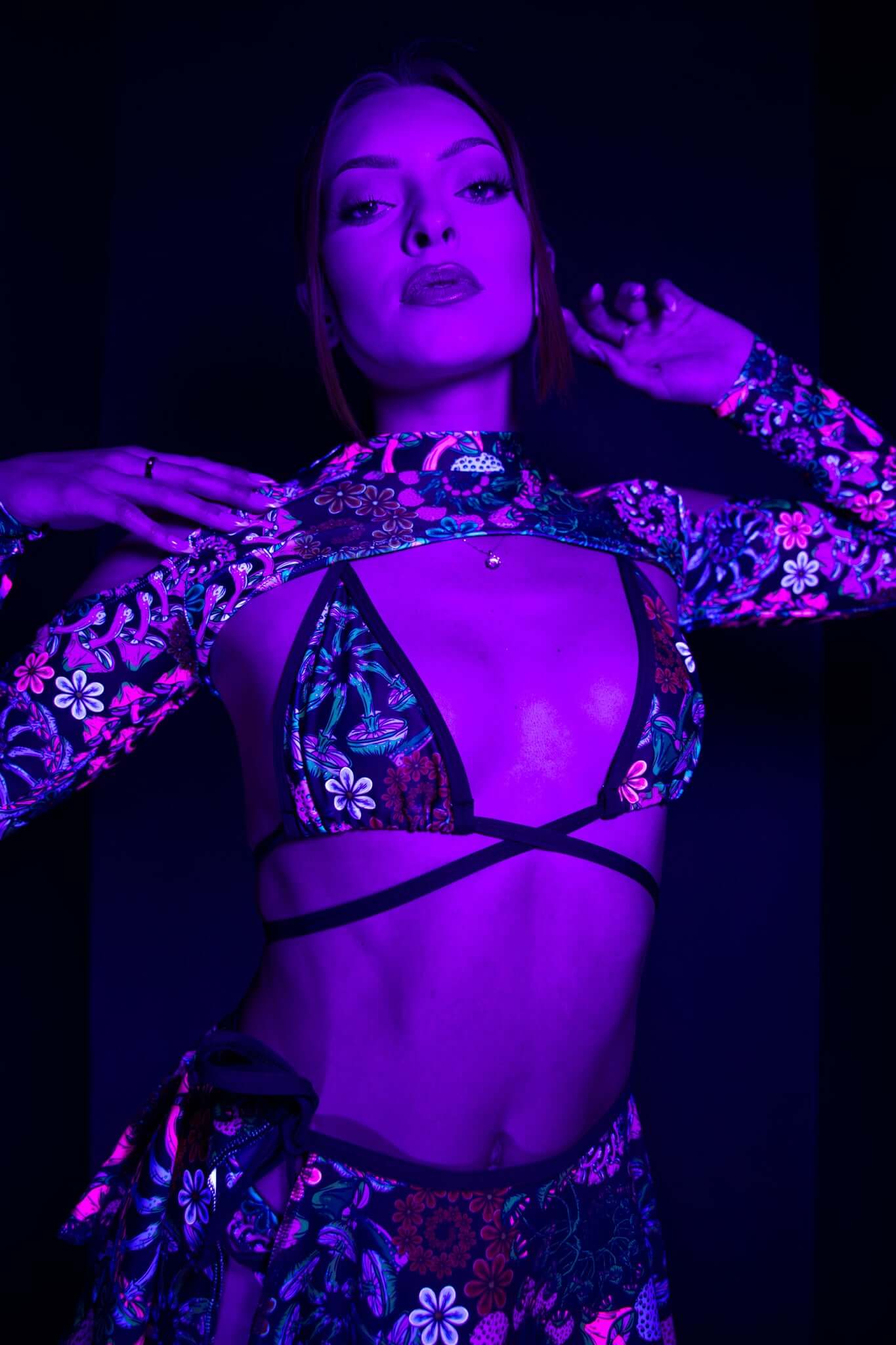 Model in Freedom Rave Wear's psychedelic print bikini top and skirt, accented by crisscross straps and purple lighting, exuding bold rave style.