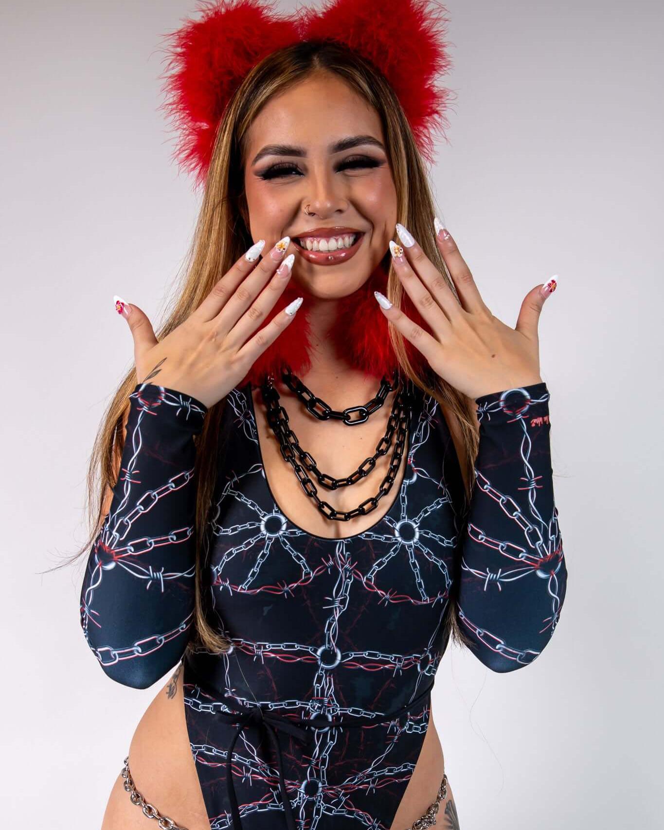 Smiling model showcasing a black and chain-patterned bodysuit, adorned with red furry ear accessories and layered chains.