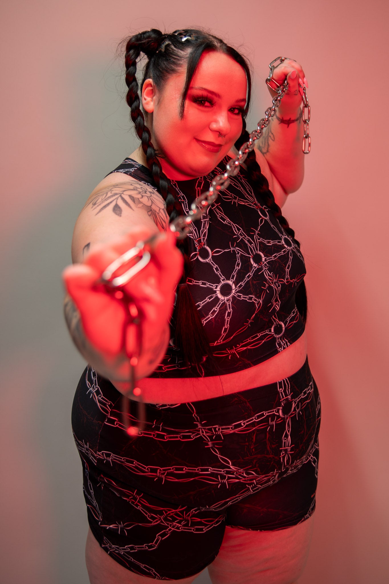 Model wearing Purgatory Crop Top with chain and barbed wire pattern, sleeveless high-neck design, shown in vibrant red lighting.