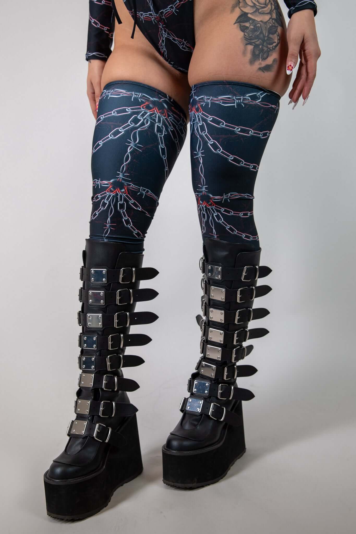 Front view of Purgatory Leg Sleeves. Chain and barbed wire print, high-thigh fit, and stretchy design for edgy rave and festival style