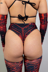 Rear view of a woman in a black and red Freedom Rave Wear high-waisted bottom featuring a circuit design, tied at the back, paired with matching arm sleeves