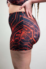 Side view of Freedom Rave Wear high-waisted shorts in red and black circuit design, modeled with a braided hairstyle against a neutral backdrop